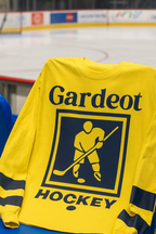 Yellow hockey jersey with 'Gardeot Hockey' branding on a blue bench at a hockey rink.
