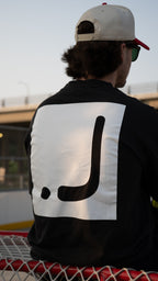 Person wearing a black jacket with a large white logo on the back, sitting on a red and black surface.